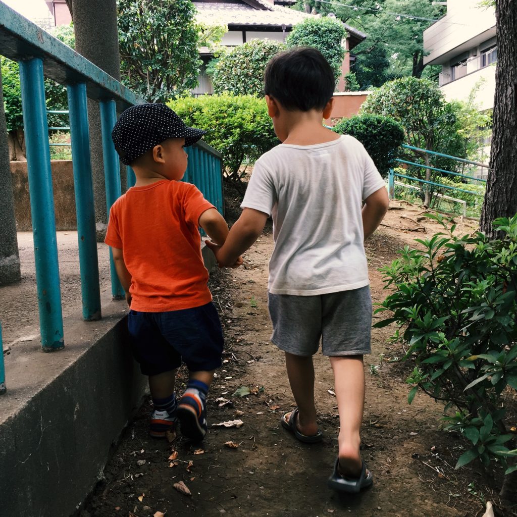 公園で手をつなぐ男の子ふたり。2歳と3歳。