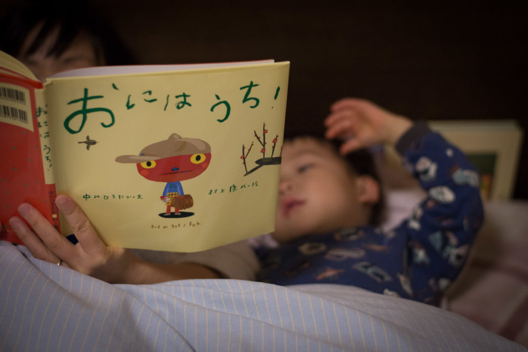 ママと一緒にベッドで絵本を読んでいる3歳の息子