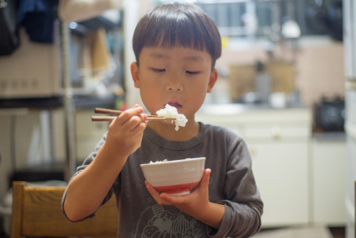 お茶碗を持ってお箸でごはんを食べる5歳の男の子
