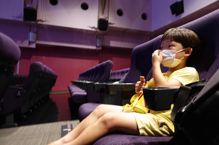 マスクをつけて映画館のシートに座る6歳の息子