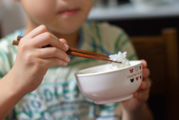お箸と茶碗でごはんをたべる7歳の息子