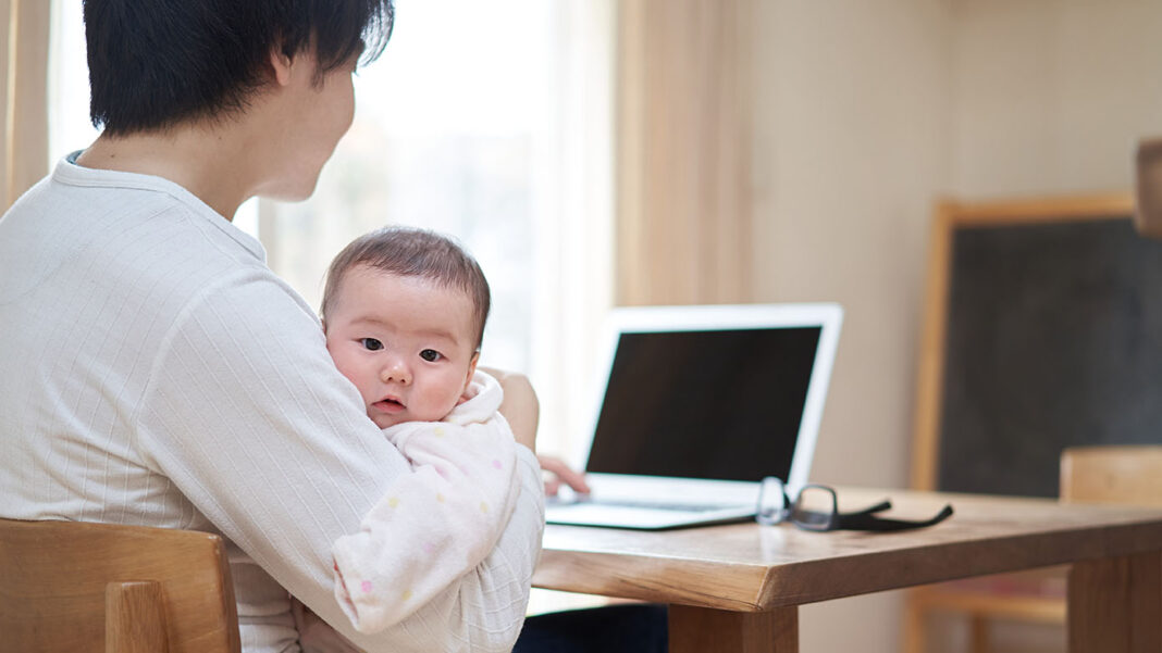 赤ちゃんを抱っこしながら、パソコンで検索する父親