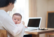 赤ちゃんを抱っこしながら、パソコンで検索する父親
