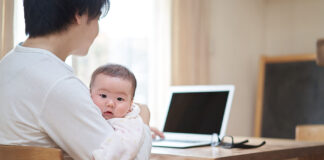 赤ちゃんを抱っこしながら、パソコンで検索する父親